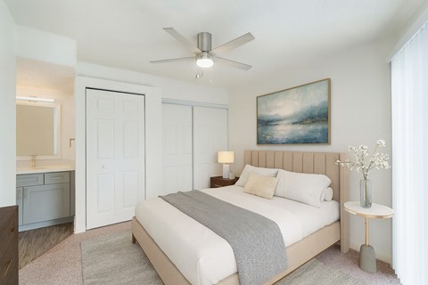 A bedroom with a large bed, a ceiling fan, and a painting on the wall.