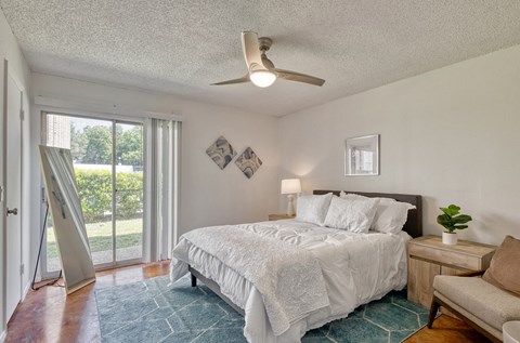 Bedroom with brown concrete floors, white walls, a ceiling fanand sliding glass doors to a balcony