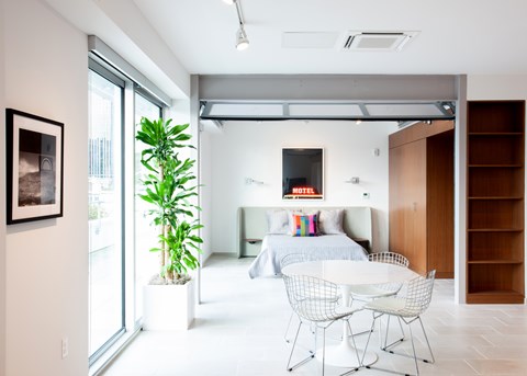 A modern bedroom with a bed, a chair, and a plant.