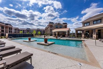 A swimming pool surrounded by sun loungers and apartment buildings.