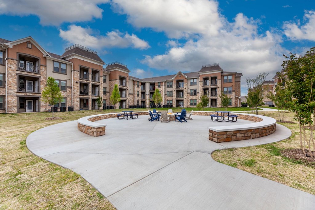 A large concrete patio with a circular design and a few benches in front of apartment buildings.