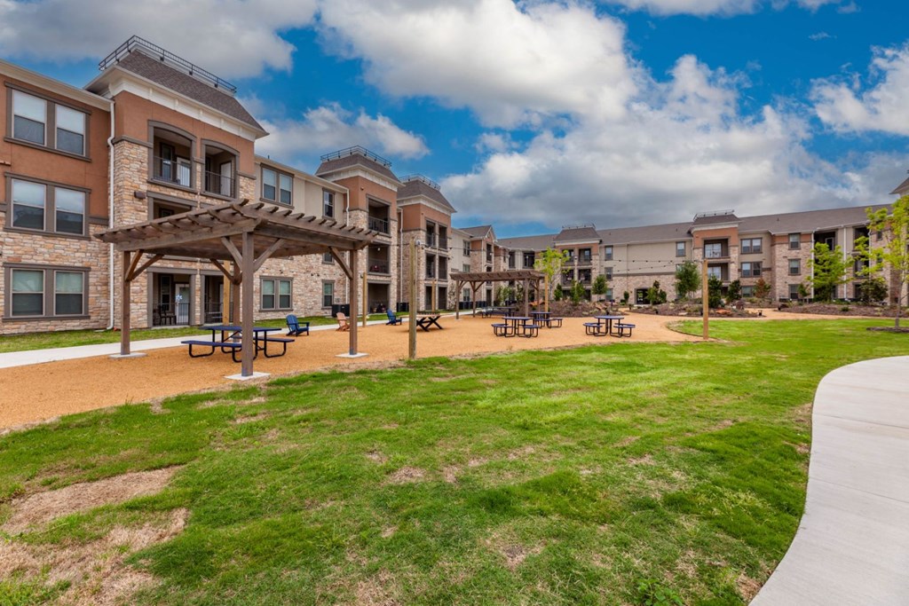 A large grassy area in front of apartment buildings with picnic tables.
