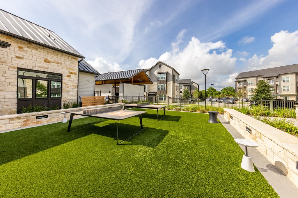 A table tennis table is in the middle of a grassy area.