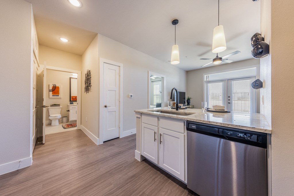 A kitchen with a stainless steel dishwasher and white cabinets.