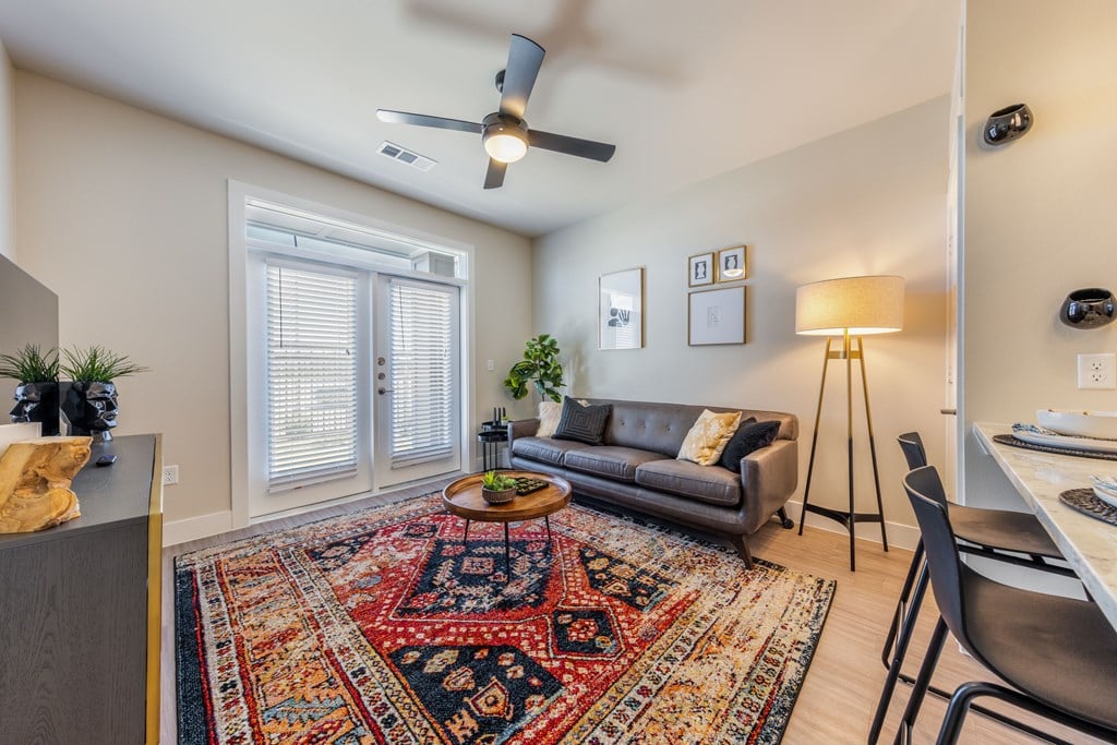 A living room with a rug, a couch, a table, and a ceiling fan.
