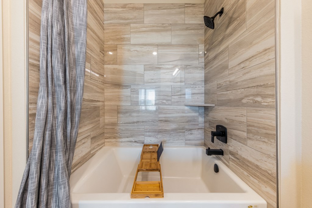 A bathroom with a marble wall and a wooden tray on the bathtub.