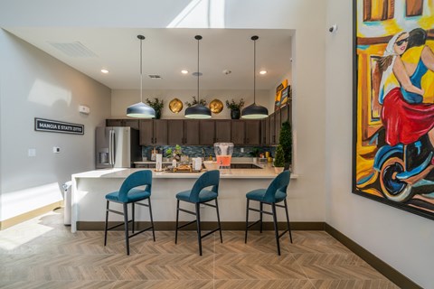 a kitchen with a bar and blue chairs and a painting on the wall