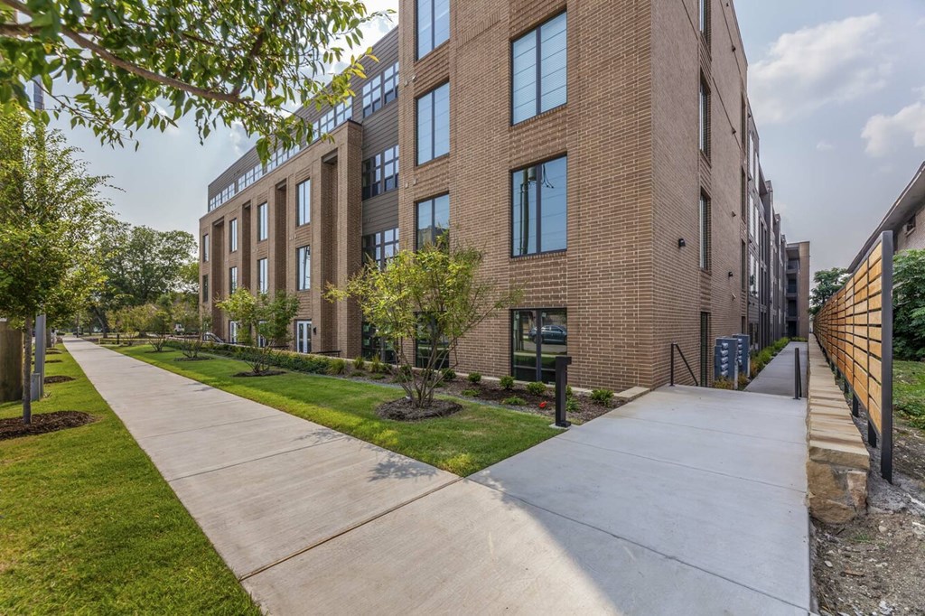 A long concrete walkway leads to a brick building with a green lawn on the side.