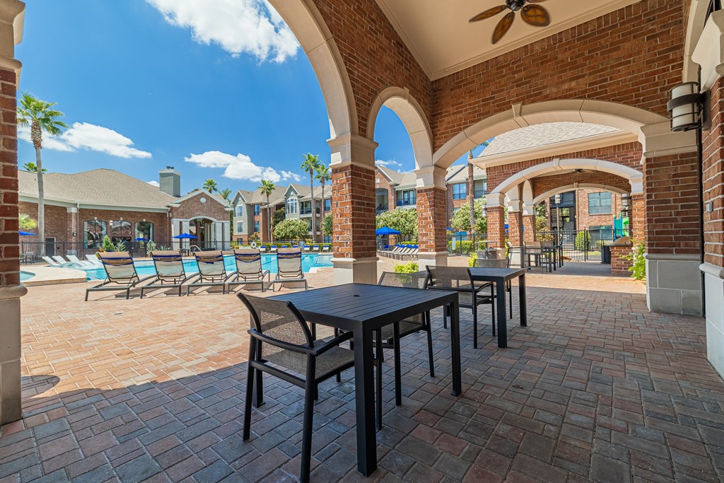 a patio with tables and chairs and a pool in the background