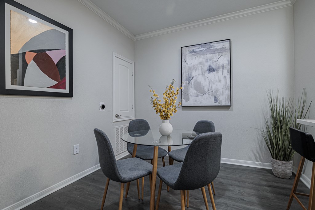 a dining room with a round table with four chairs and a vase with yellow flowers on
