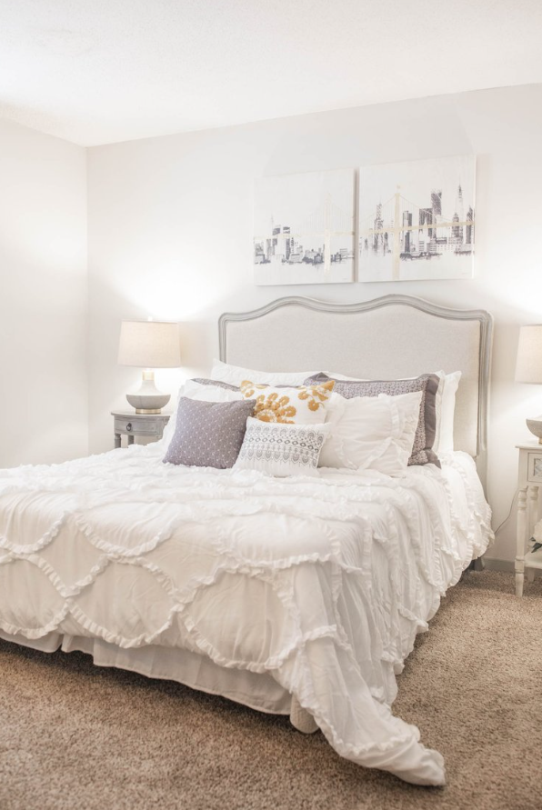 a white bedroom with a bed and pillows and a painting on the wall