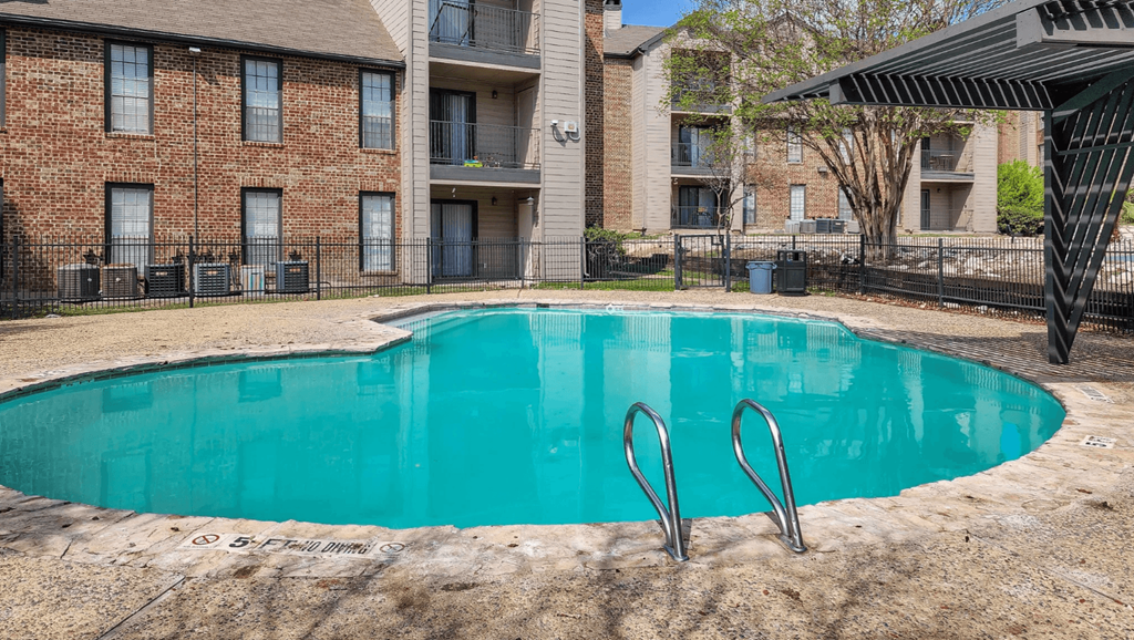 A small pool with a diving board in front of a brick building.