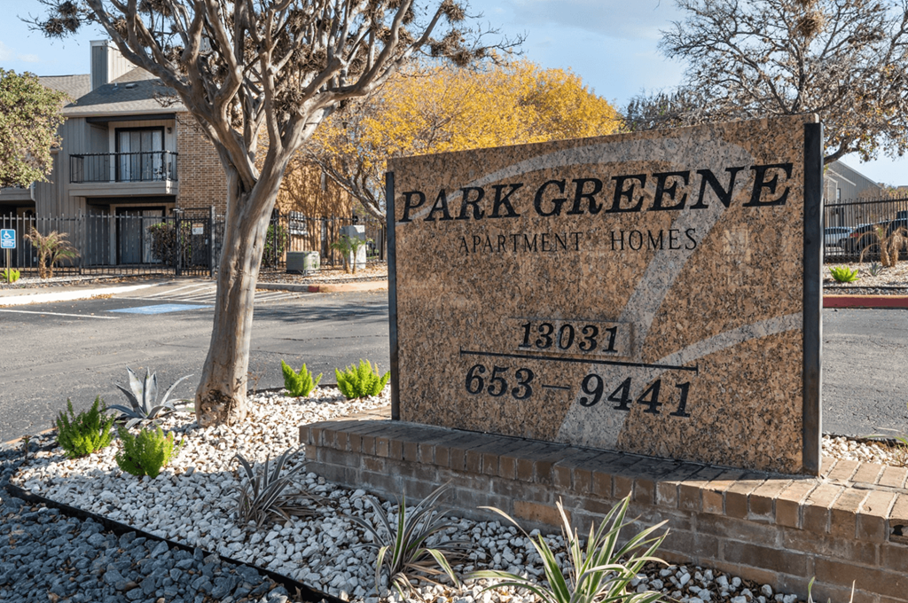 A sign for Park Greene Apartment Homes is displayed in front of a tree.
