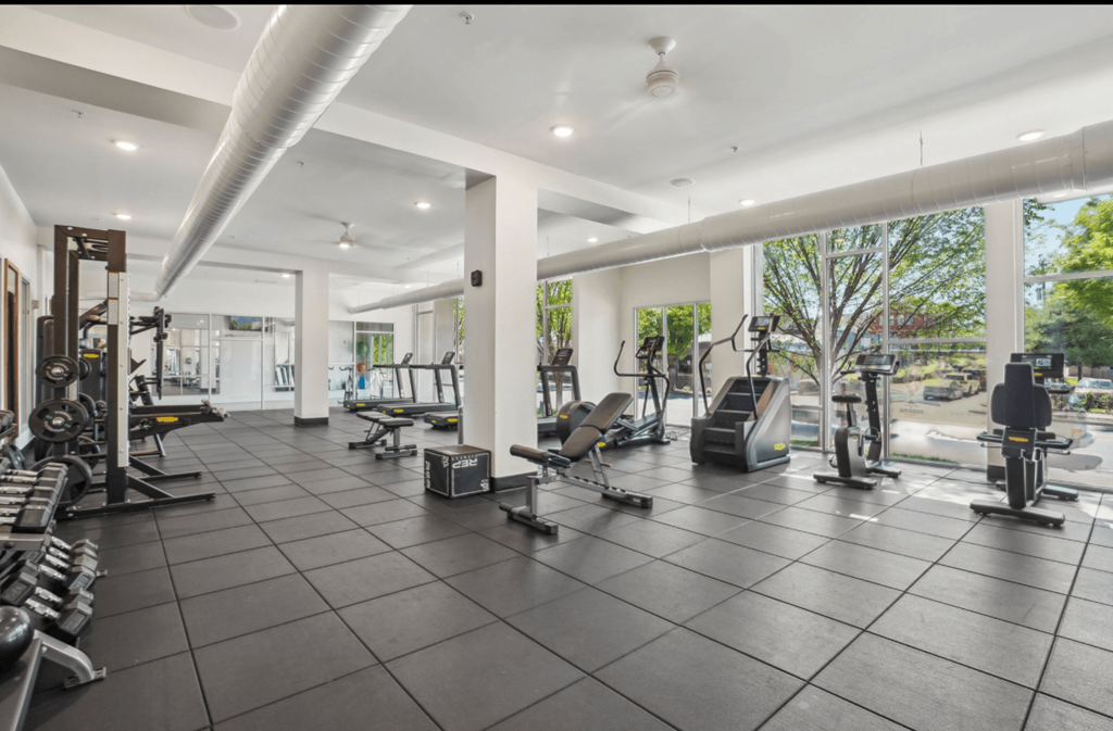 A spacious gym with various exercise equipment and a large mirror on the wall.