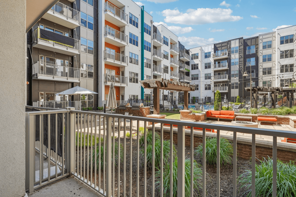 A balcony with a metal railing overlooks a courtyard with a seating area.