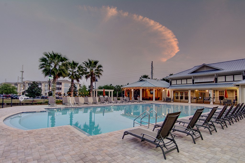 A pool surrounded by lounge chairs with a building and palm trees in the background.
