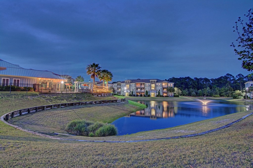 A serene landscape with a lake, a bridge, and a building with lights on.