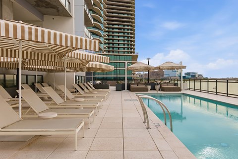 A pool area with sun loungers and a tall building in the background.