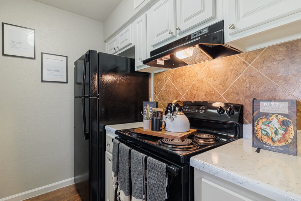 A kitchen with a black refrigerator and stove top oven.