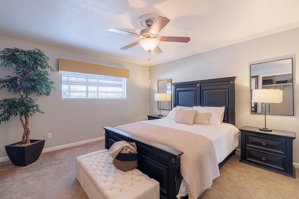 A bedroom with a large bed, a ceiling fan, and a potted plant.
