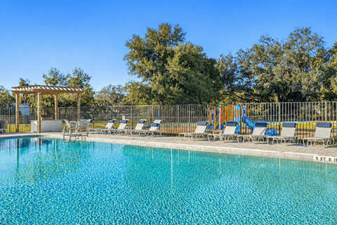 A pool with chairs and a pergola in the background.