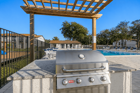 A BBQ grill is on a concrete slab with a pergola above it.
