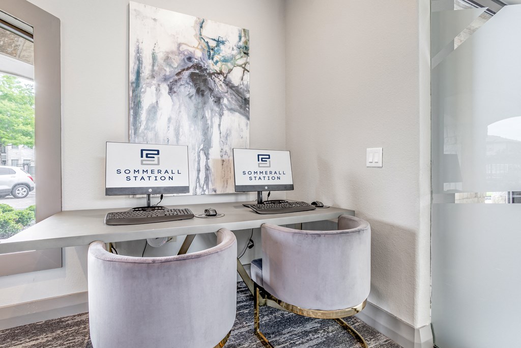 two computers sitting on a desk in a room with two chairs