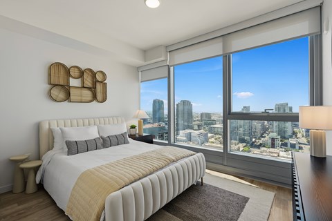 A bedroom with a large bed and a city view through the window.