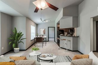 a living room with a ceiling fan and a kitchen in the background