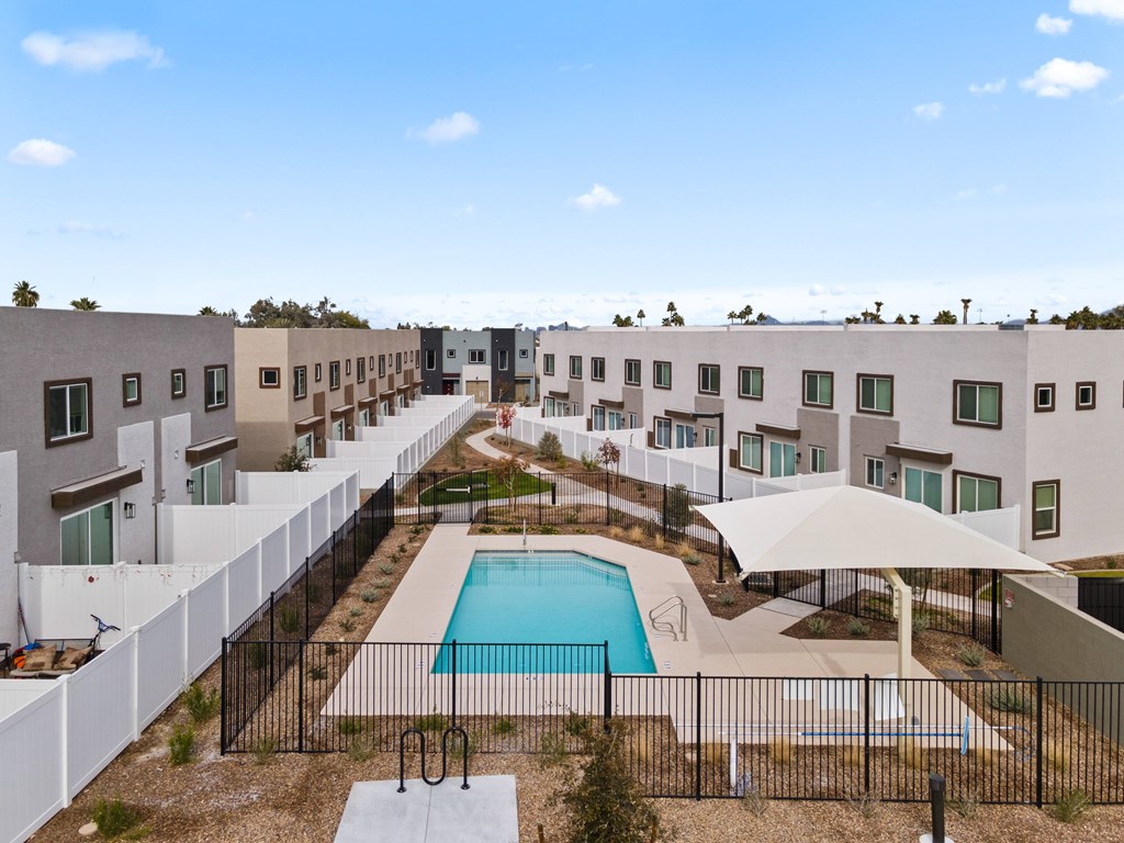 A swimming pool is surrounded by a black fence in a residential area.