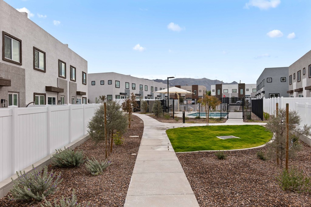 A white fence runs along the edge of a gravel area with a small green lawn and a concrete walkway.