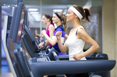 three women running on cardio machines at the gym