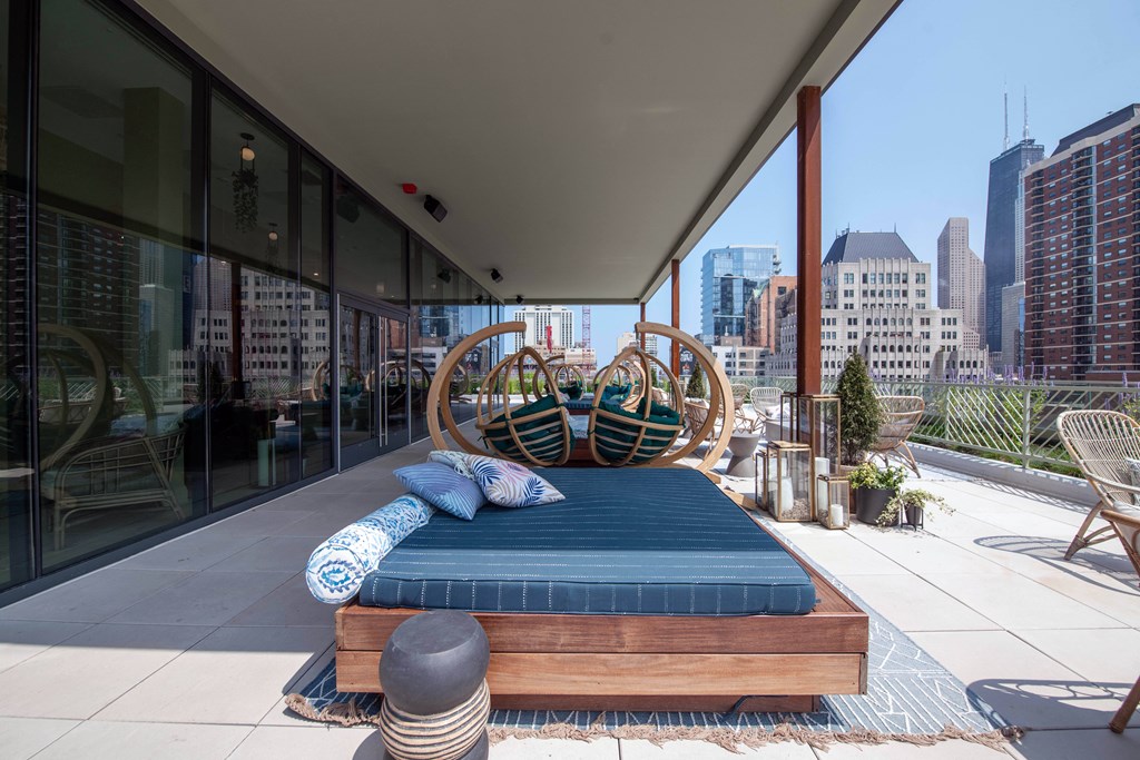A blue cushioned bench sits on a patio with a city skyline in the background.