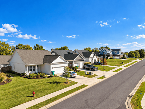 A residential street with houses on both sides and cars parked in front.