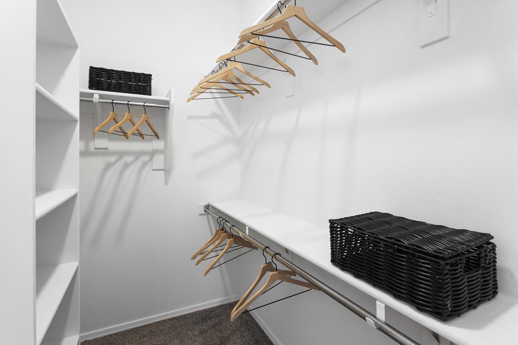 a walk in closet with a white wall and a shelf with wicker baskets