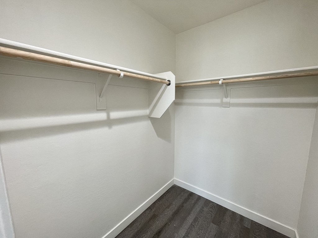 a walk in closet with white walls and a wooden floor