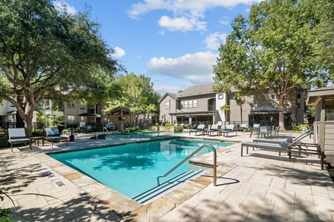 A swimming pool surrounded by trees and lounge chairs.