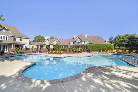 A large swimming pool surrounded by lounge chairs and a building in the background.