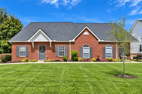A red brick house with a grey roof and a green lawn in front.