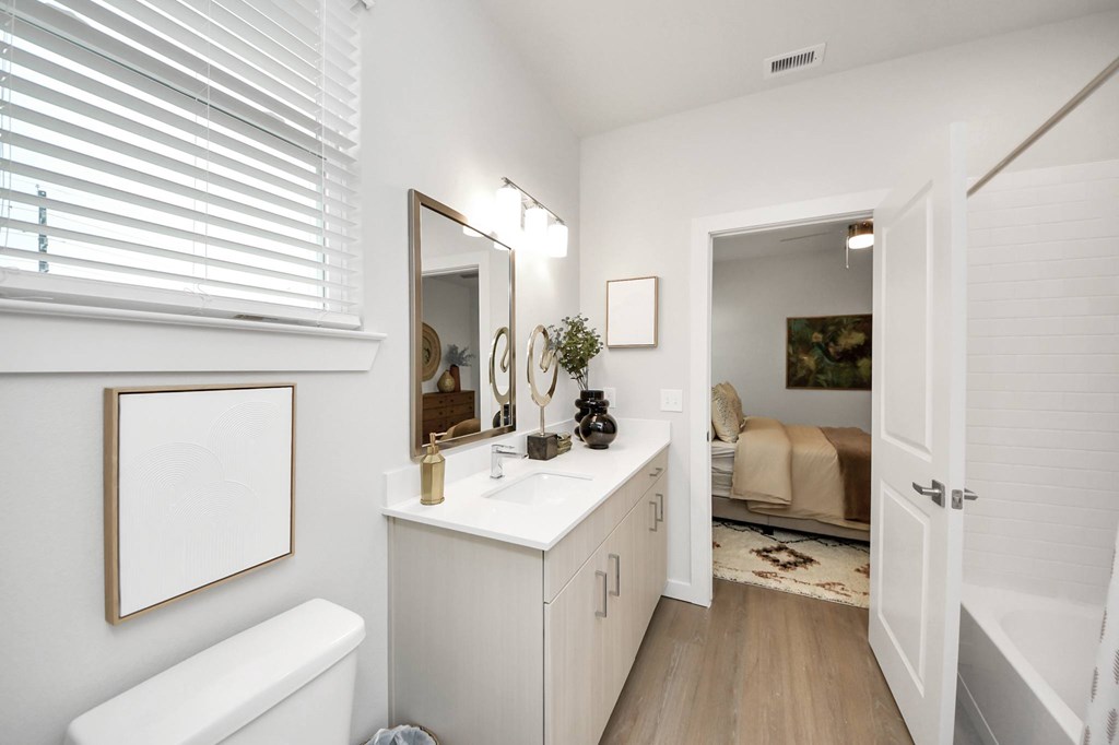 A white bathroom with a toilet, sink, mirror, and a picture frame on the wall.