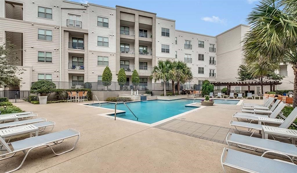 a large swimming pool with white chairs in front of an apartment building