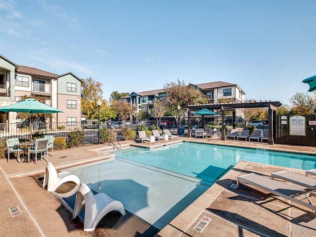a swimming pool with chairs and umbrellas at an apartment complex
