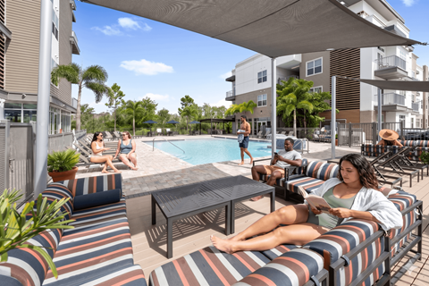 A woman is sitting on a striped couch by a pool.