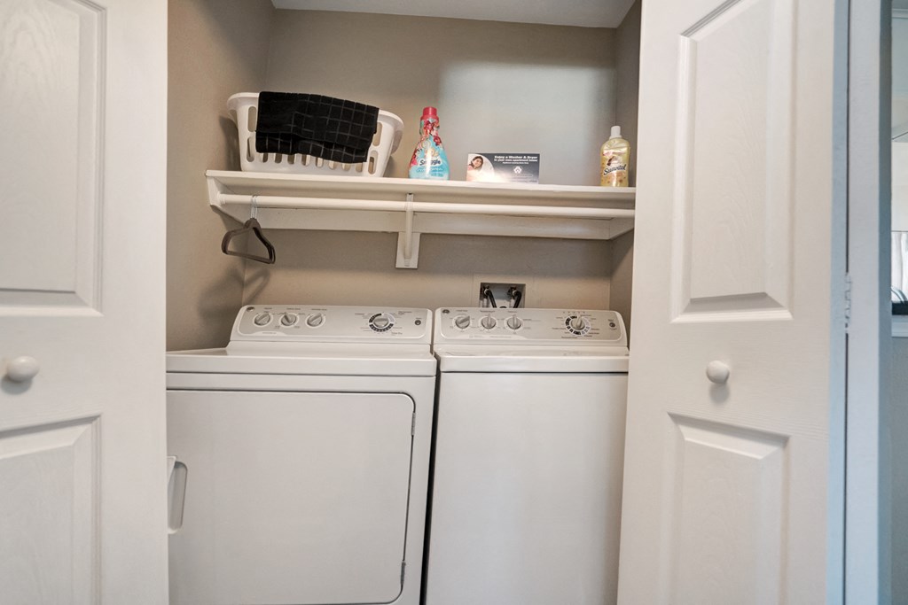 A white laundry room with two washing machines and a shelf above them.