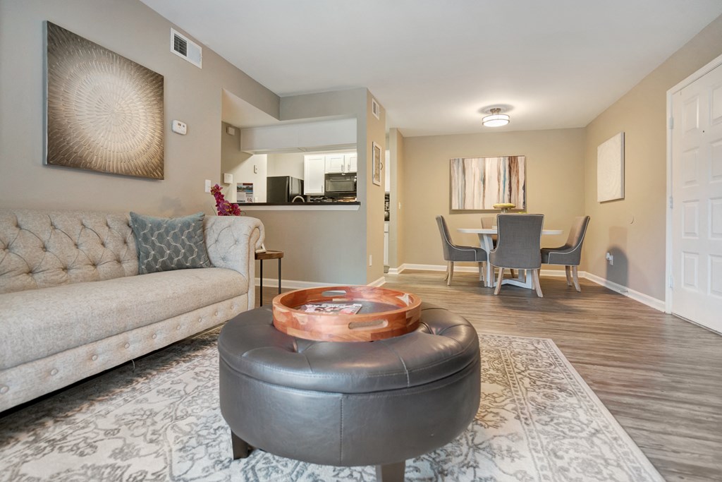 A living room with a grey ottoman and a grey couch with a wooden coffee table in front of it.