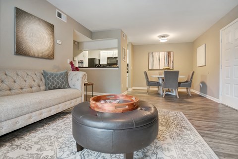 A living room with a grey ottoman and a grey couch with a wooden coffee table in front of it.