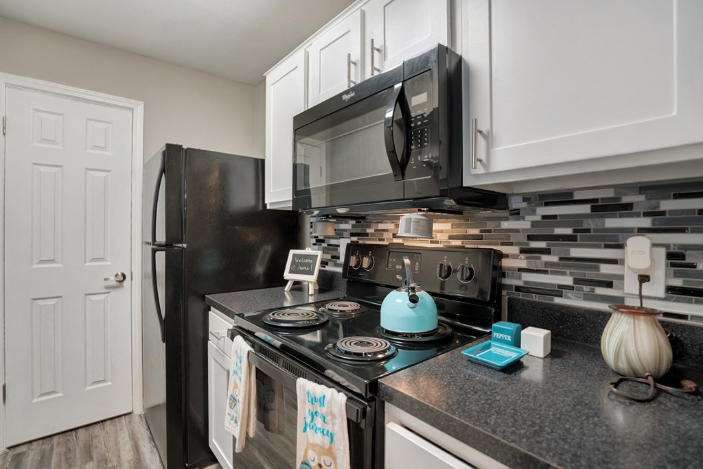 A black refrigerator and microwave in a kitchen with a white door.