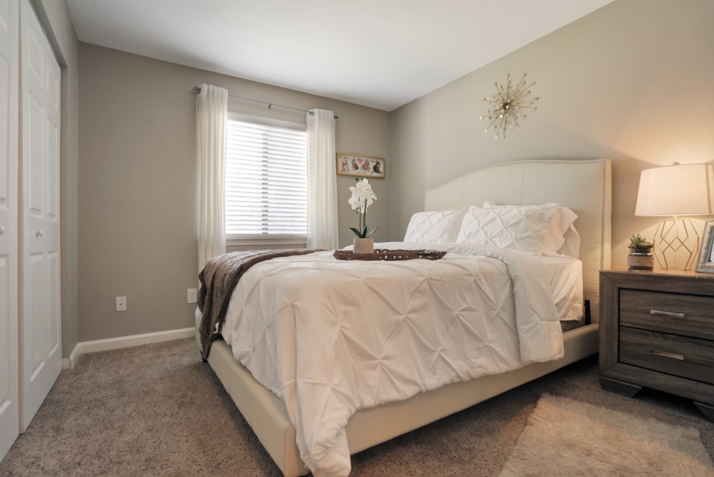 A bedroom with a large bed and a nightstand with a lamp.