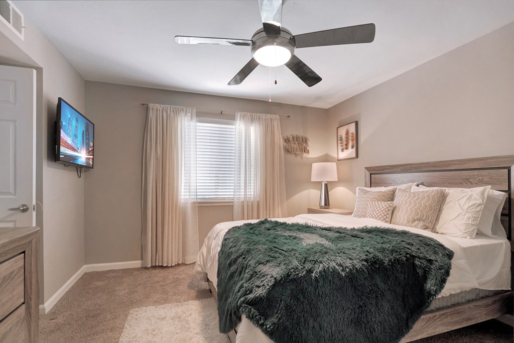 A bedroom with a bed, a ceiling fan, and a television mounted on the wall.