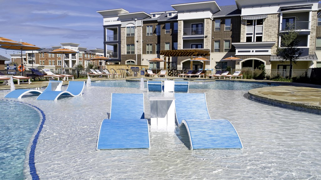 a large swimming pool with blue chairs in front of an apartment building